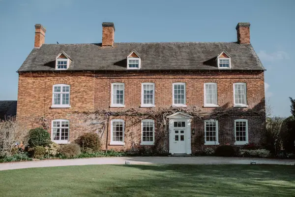 Charming red-brick mansion with elegant windows, lush gardens, and inviting entrance—ideal for intimate wedding celebrations.