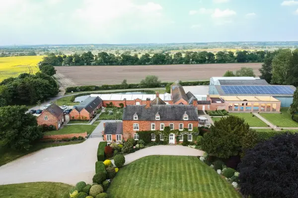 Aerial view of a charming wedding venue featuring manicured gardens, rustic brick buildings, and a scenic countryside backdrop.
