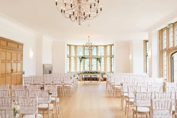 Bright ceremony space featuring elegant chairs arranged in rows, large windows providing natural light, and a stunning chandelier.
