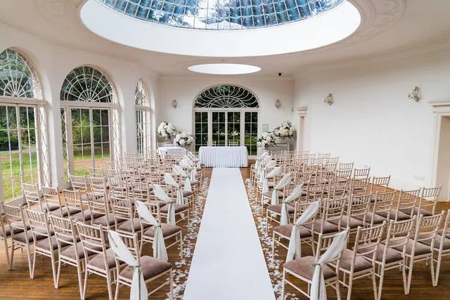 Elegant ceremony space featuring rows of chiavari chairs, a floral arrangement backdrop, and a stunning skylight overhead.