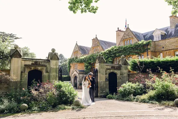 Couple embraces in front of a charming stone estate, surrounded by lush gardens and historic architecture, creating a romantic wedding backdrop.