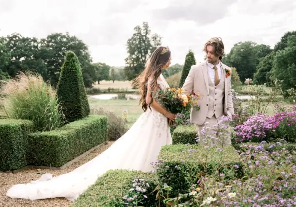 A couple gazes at each other in a lush garden, surrounded by manicured hedges and vibrant flowers, perfect for a romantic outdoor wedding.
