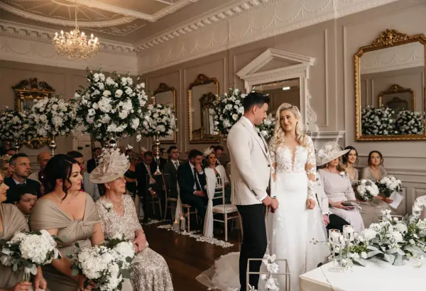 Intimate ceremony in an elegant indoor venue, featuring lush floral arrangements, vintage decor, and an engaged couple exchanging vows.