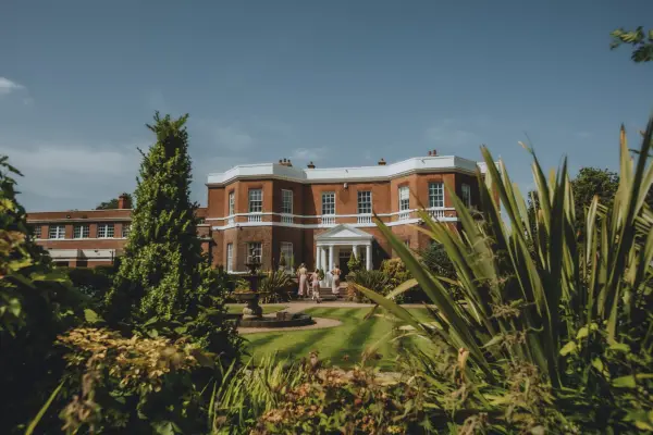 Stunning red brick mansion surrounded by lush gardens and vibrant greenery, offering a picturesque backdrop for outdoor weddings.