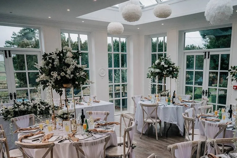 Bright, airy reception space with elegant round tables, floral centerpieces, and large windows, creating a serene, romantic atmosphere.