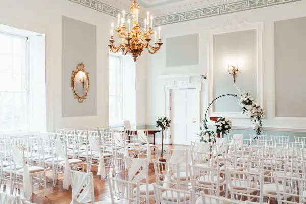 Bright, elegant ceremony space with white chiavari chairs, a grand chandelier, and floral accents, perfect for a romantic wedding.