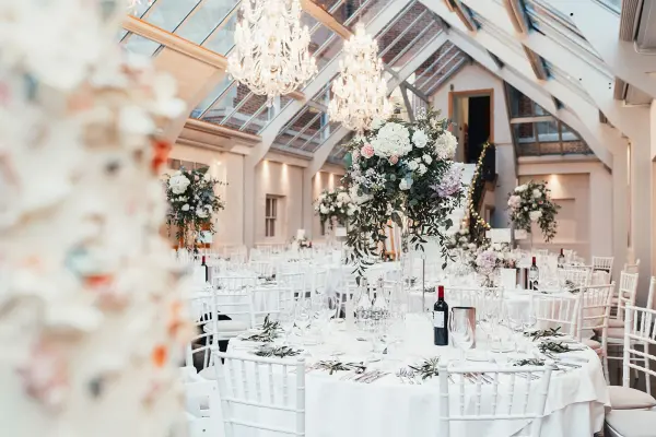 Elegant reception room featuring glass ceilings, chic chandeliers, and beautifully arranged tables adorned with floral centerpieces.