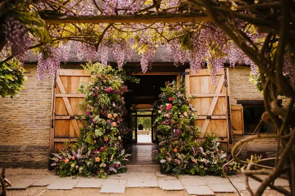 Charming entrance featuring rustic wooden doors adorned with vibrant floral arrangements and wisteria, creating a romantic atmosphere.