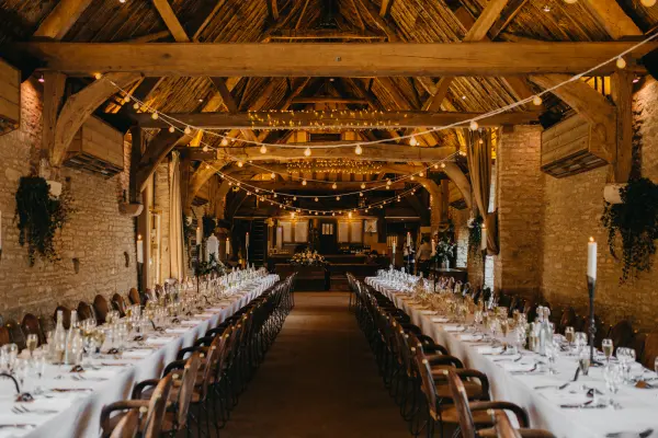 Rustic barn interior featuring long tables set for a wedding reception, adorned with candles and string lights, creating a warm ambiance.