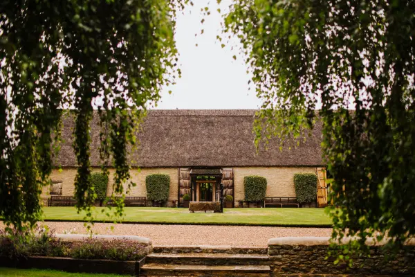 Charming rustic barn framed by lush greenery, featuring a serene outdoor space and inviting pathway for idyllic wedding celebrations.